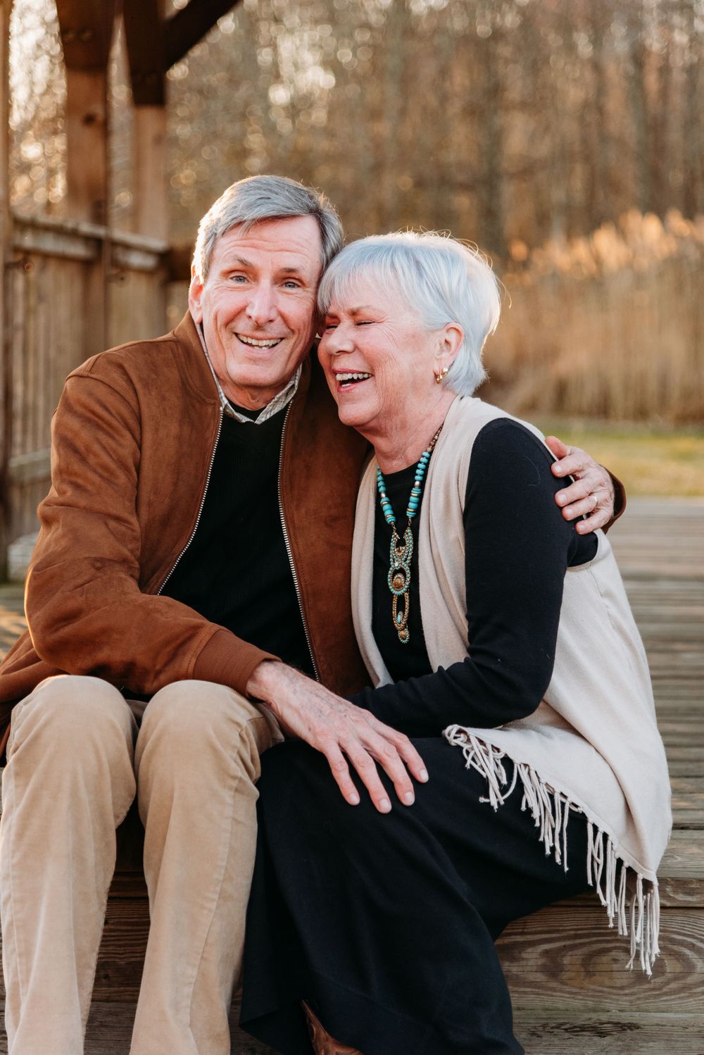 Senior couple sharing genuine laughter while sitting close together on a wooden deck.
