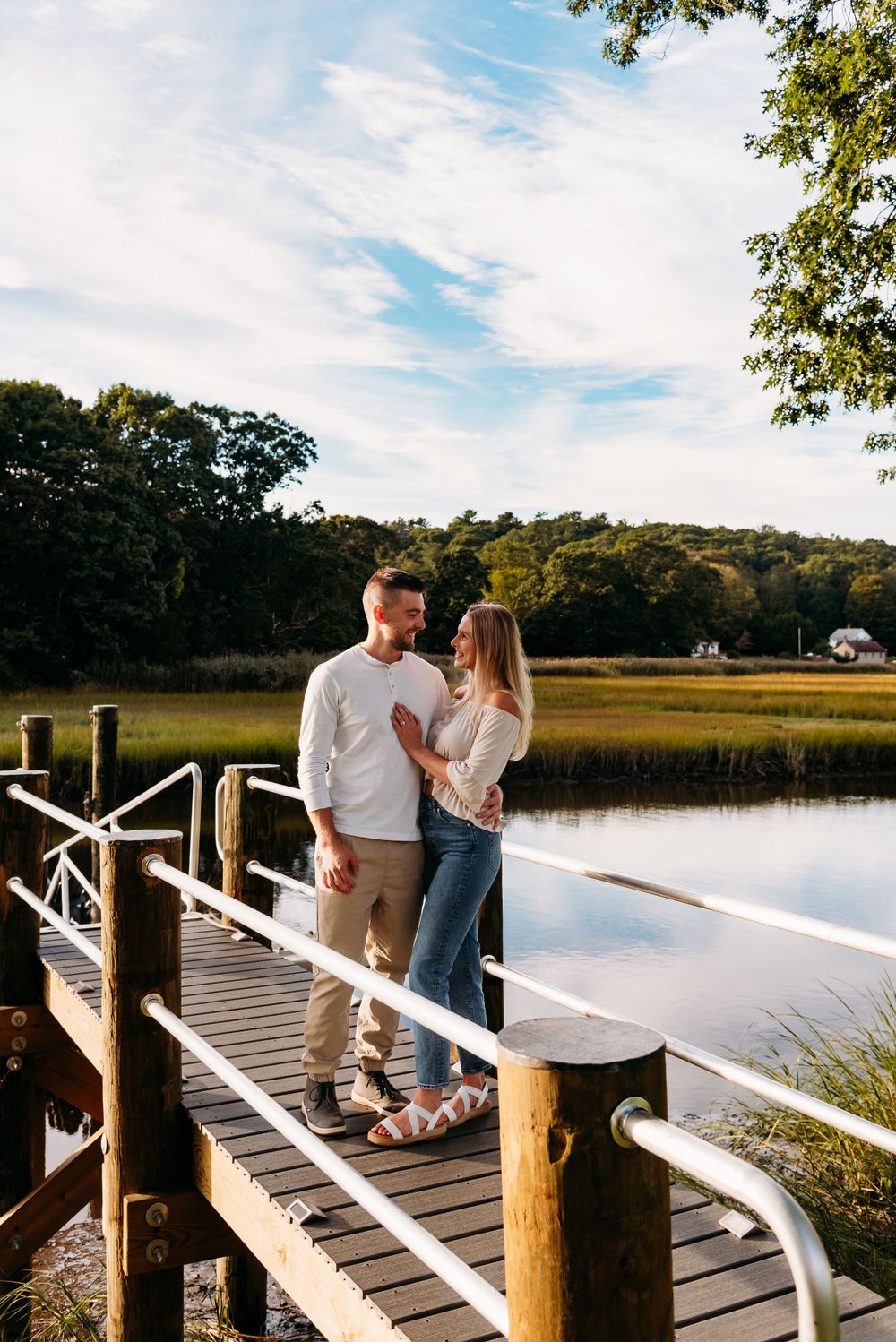 A couple stands together on a wooden dock overlooking a tranquil marsh at sunset.