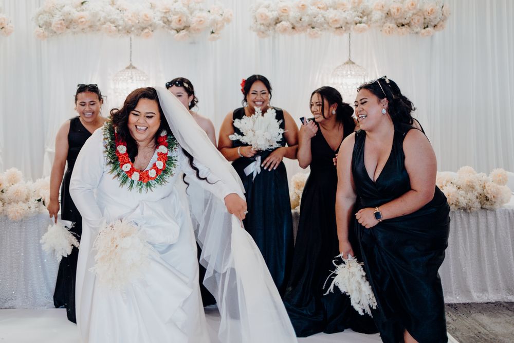 Wedding party in black and white attire celebrating in front of floral wall decor.