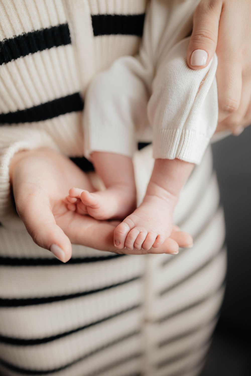 Close up of tiny baby feet being gently held by adult hands against a black and white striped sweater background.