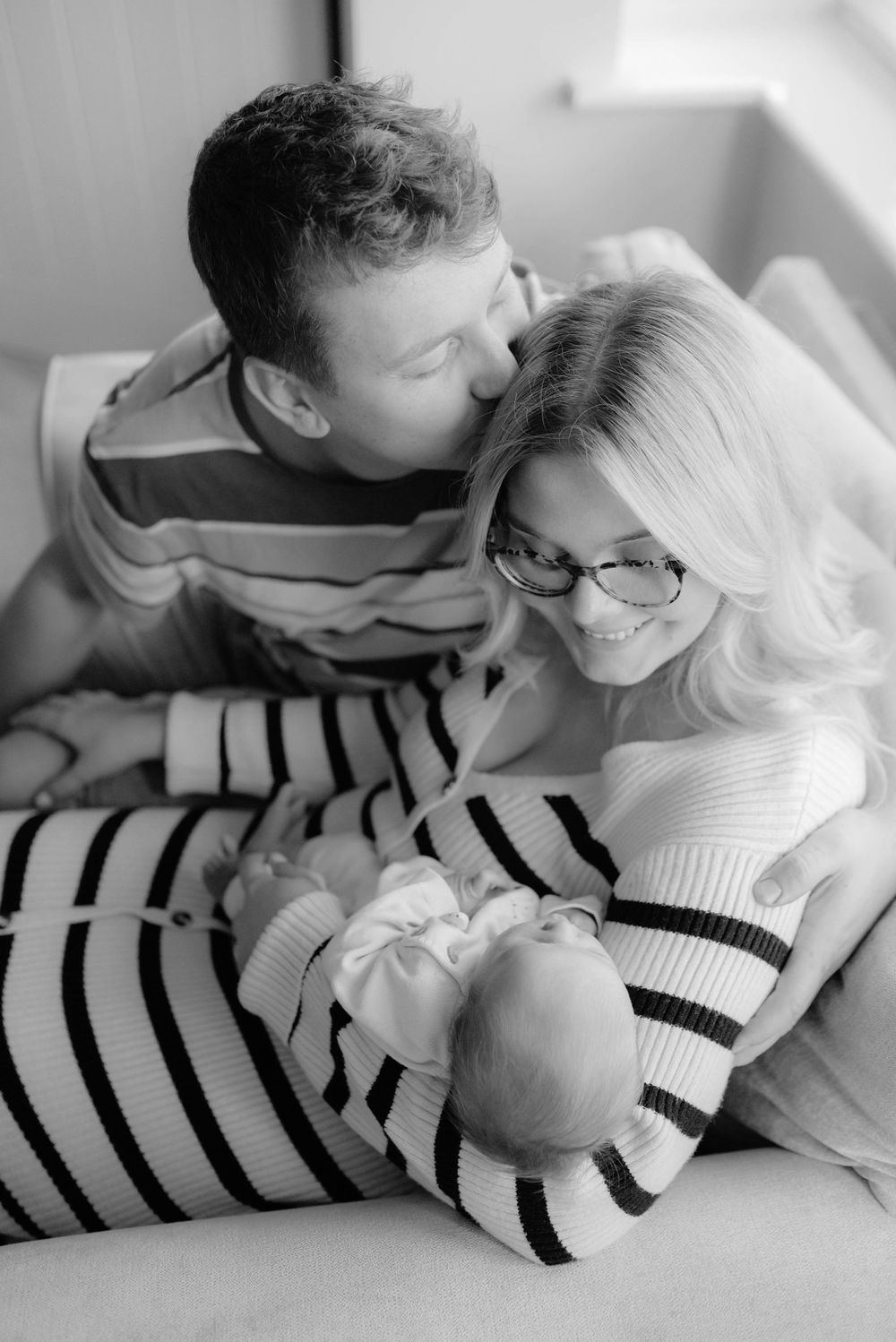 Black and white portrait of a couple looking lovingly at their newborn baby in a striped onesie.