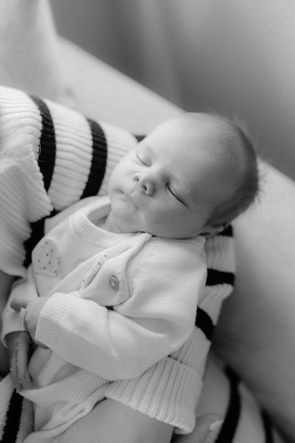 A peaceful sleeping newborn baby wearing a white and black striped sweater in a black and white photograph.