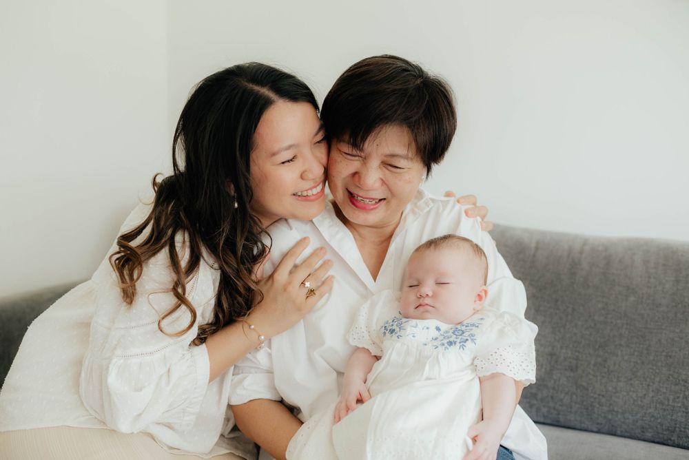 A family shares a joyful moment together while sitting on a grey couch wearing white clothing.