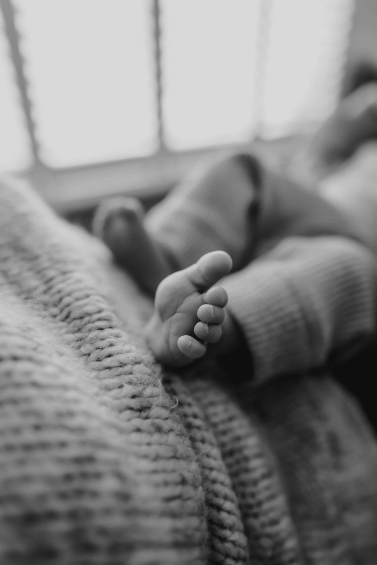 Black and white close-up of tiny baby foot resting on textured knit blanket in soft natural light.