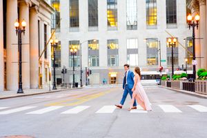 man in navy suit walking with woman in light pink dress in front of empty Chicago Board of Trade for engagement pictures