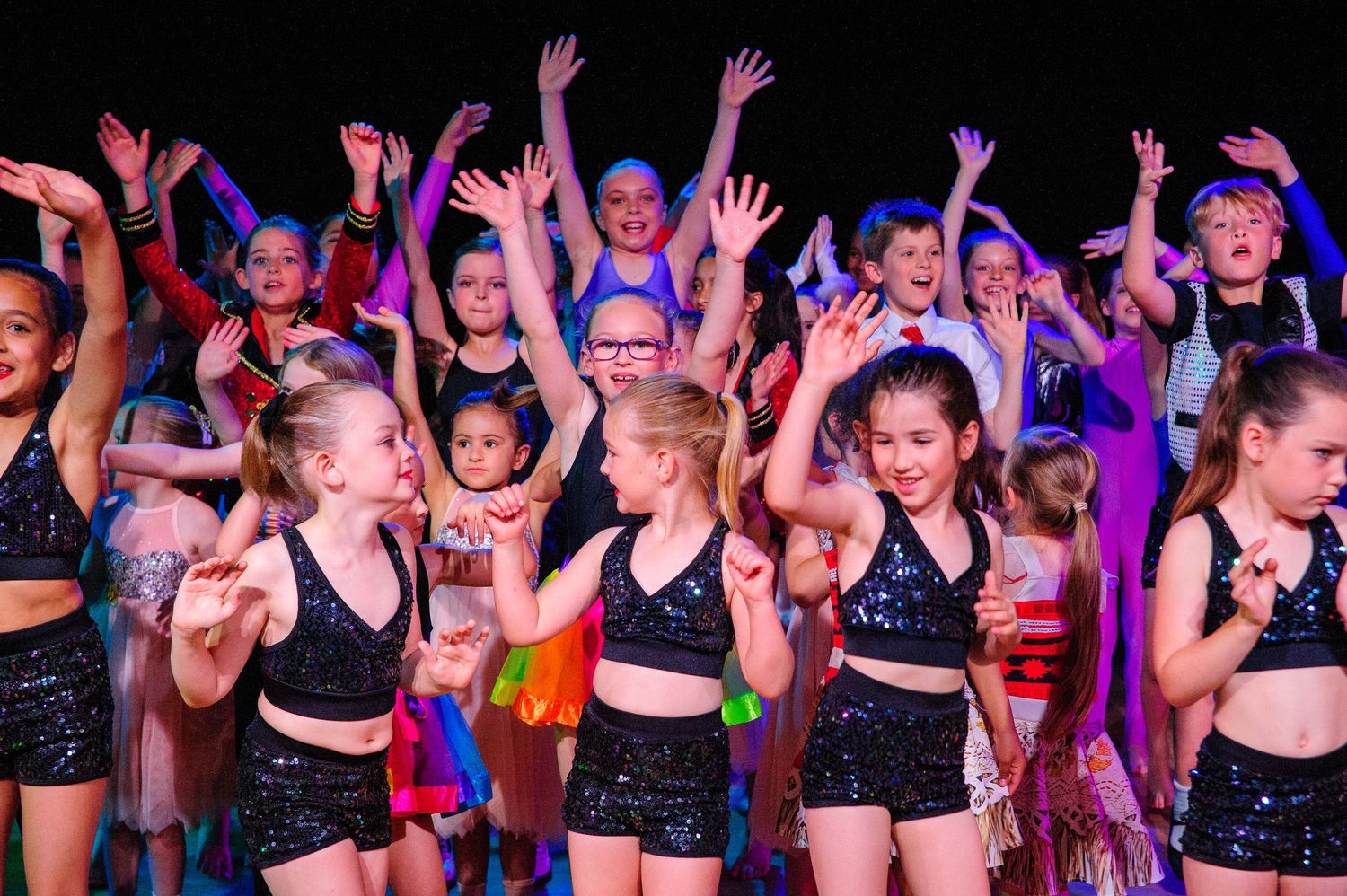 Enthusiastic young performers in black costumes with raised hands during stage show.