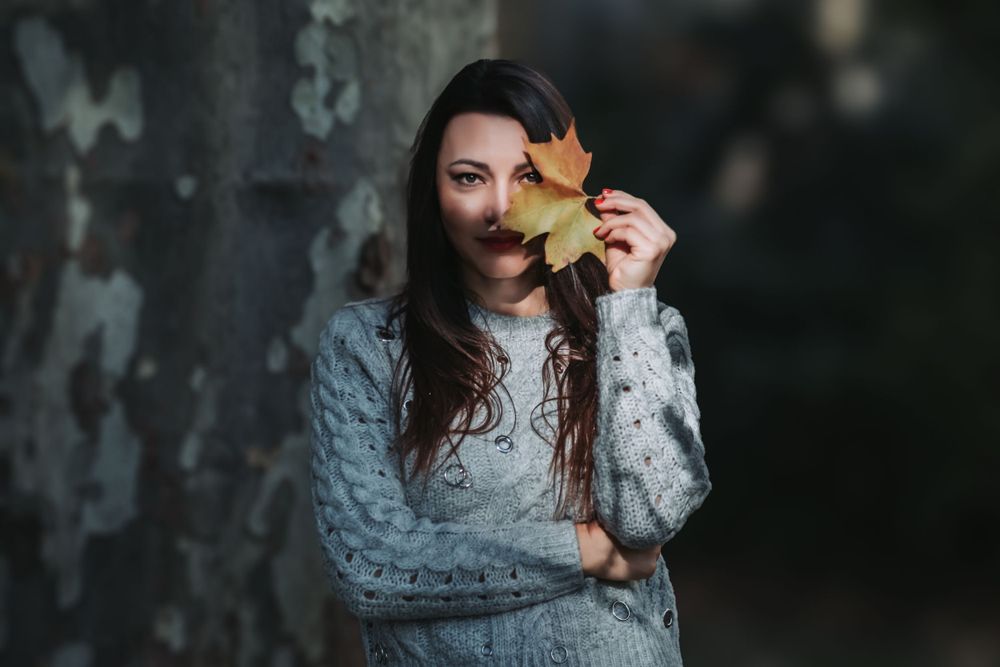 Cozy fall portrait holding yellow maple leaf while wearing gray sweater.