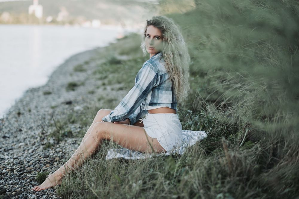 Casual outdoor photoshoot on a rocky shoreline with a plaid shirt and white shorts at sunset.