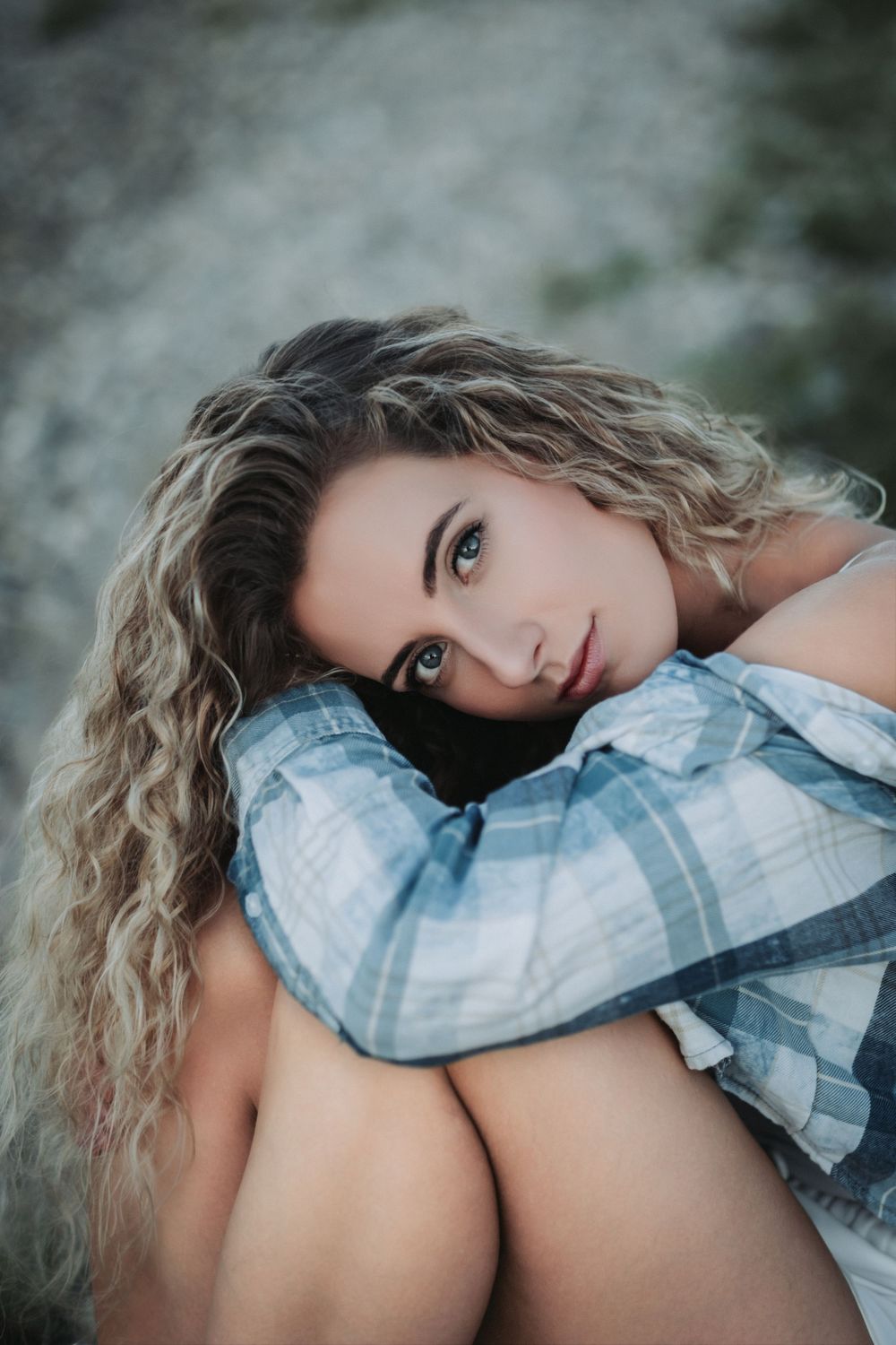 Intimate portrait on rocky ground wearing plaid shirt with curly blonde hair.