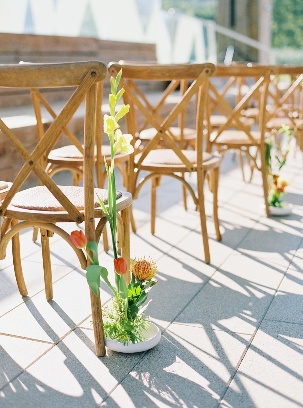 Wooden chairs with flower-filled vases on the floor at a wedding ceremony in Château La Coste, Provence.