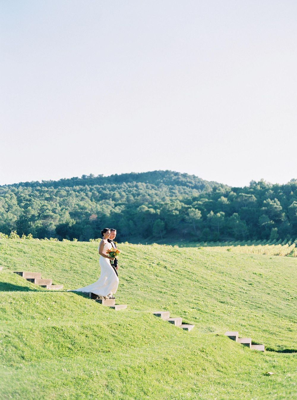A bride and her father gracefully descend a hill in a field during the bride's entrance to the ceremony.