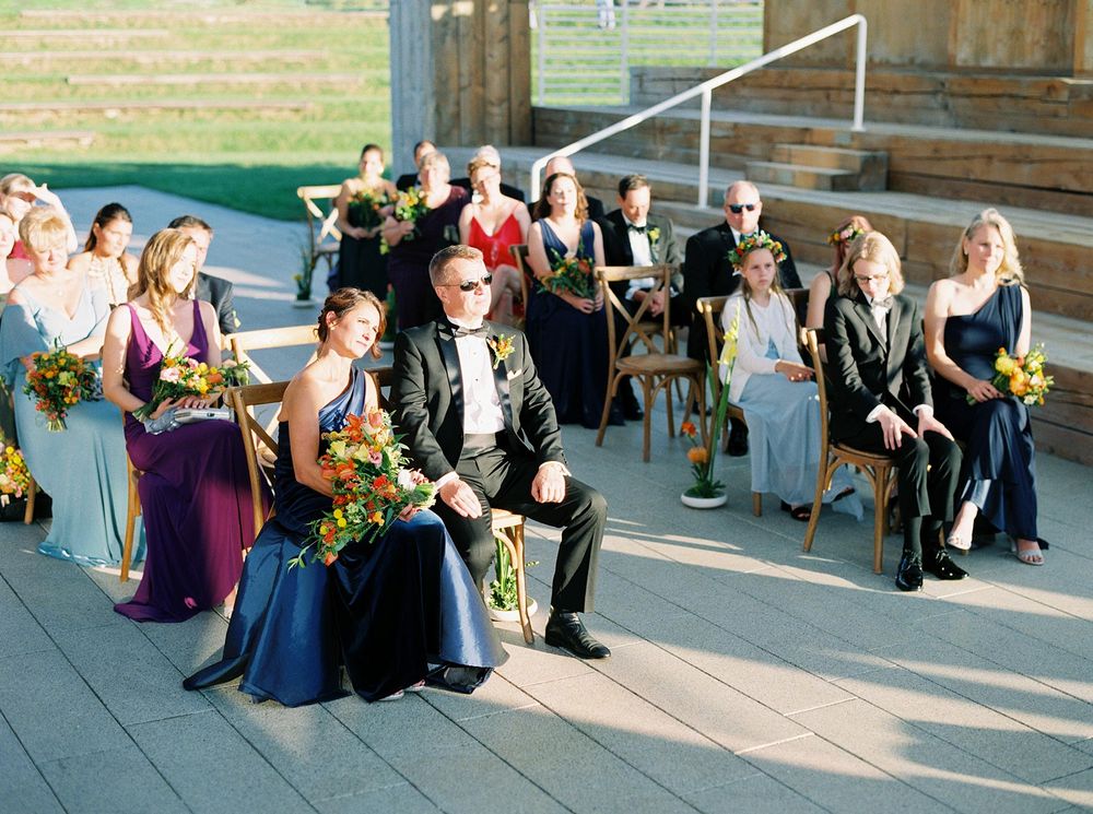 Wedding attendees seated on chairs, facing a bride and groom during the ceremony.