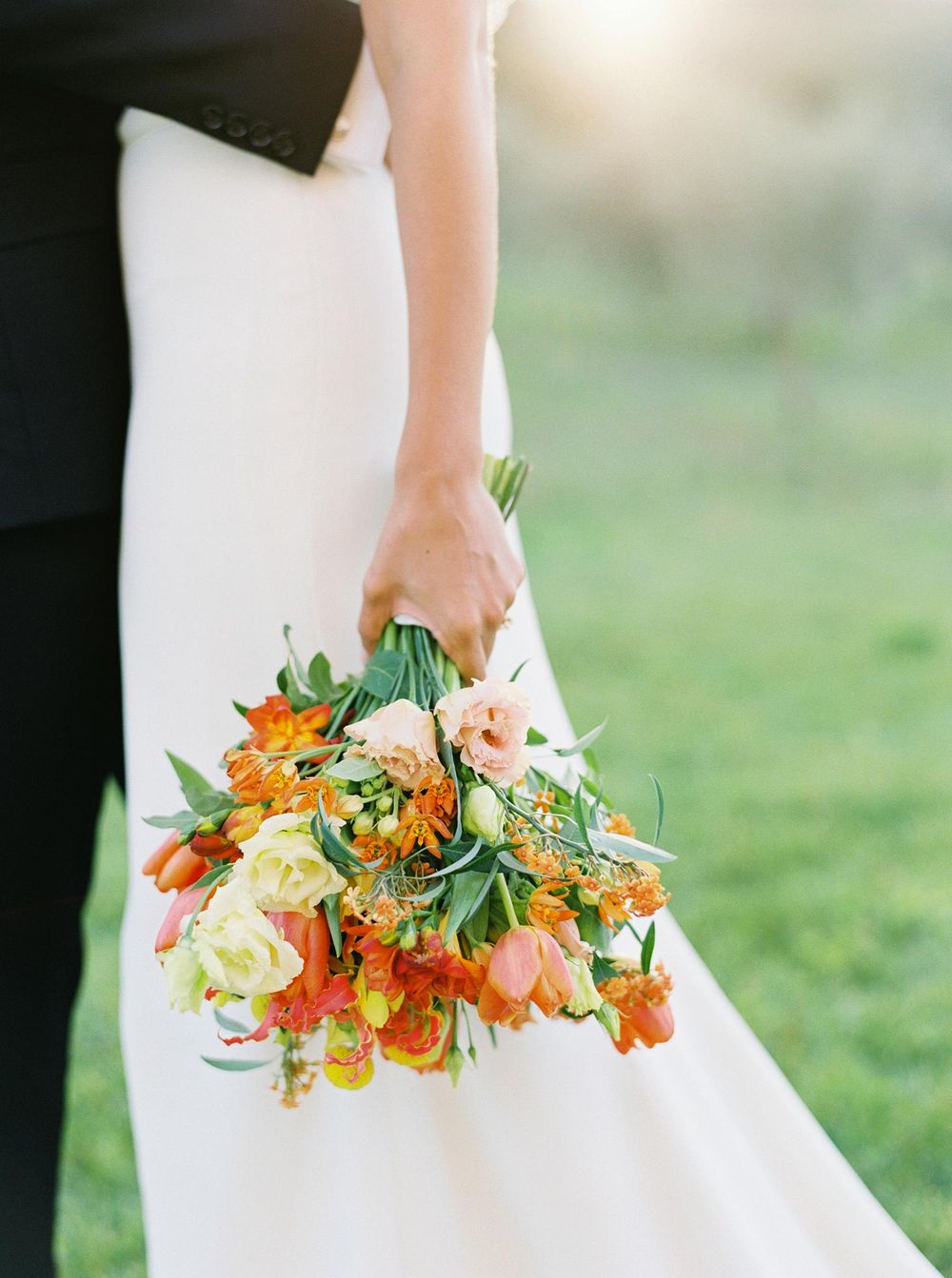 Vibrant orange and yellow wedding bouquet being held by a bride at Château La Coste, Provence.