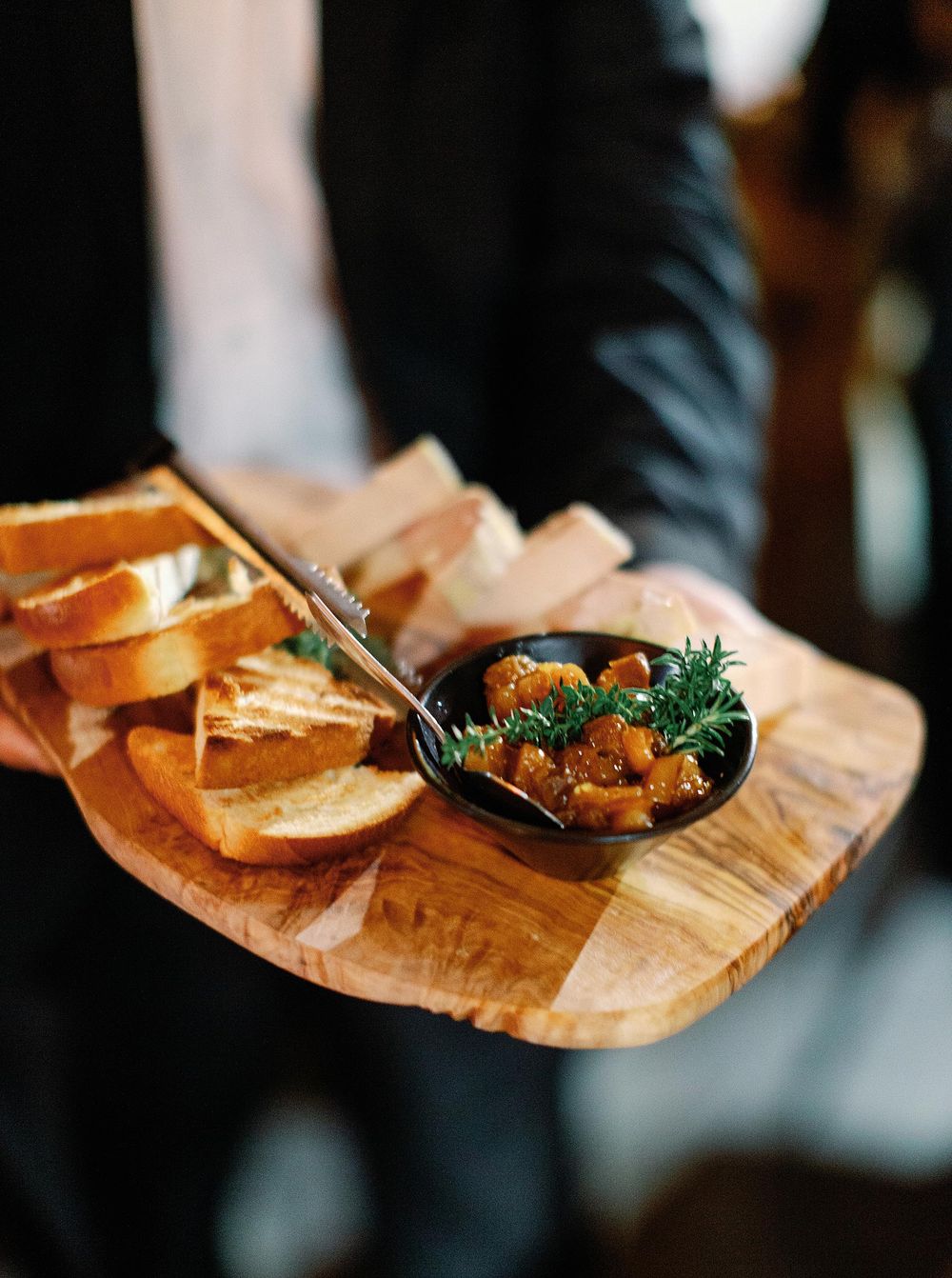 A man holding a wooden tray with bread and meat, showcasing a delicious meal with a rustic touch.