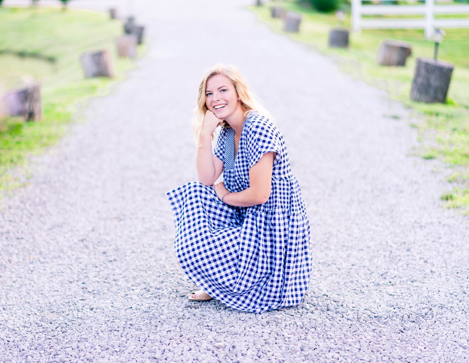 young woman in blue and white dress crouching on gravel path and smiling