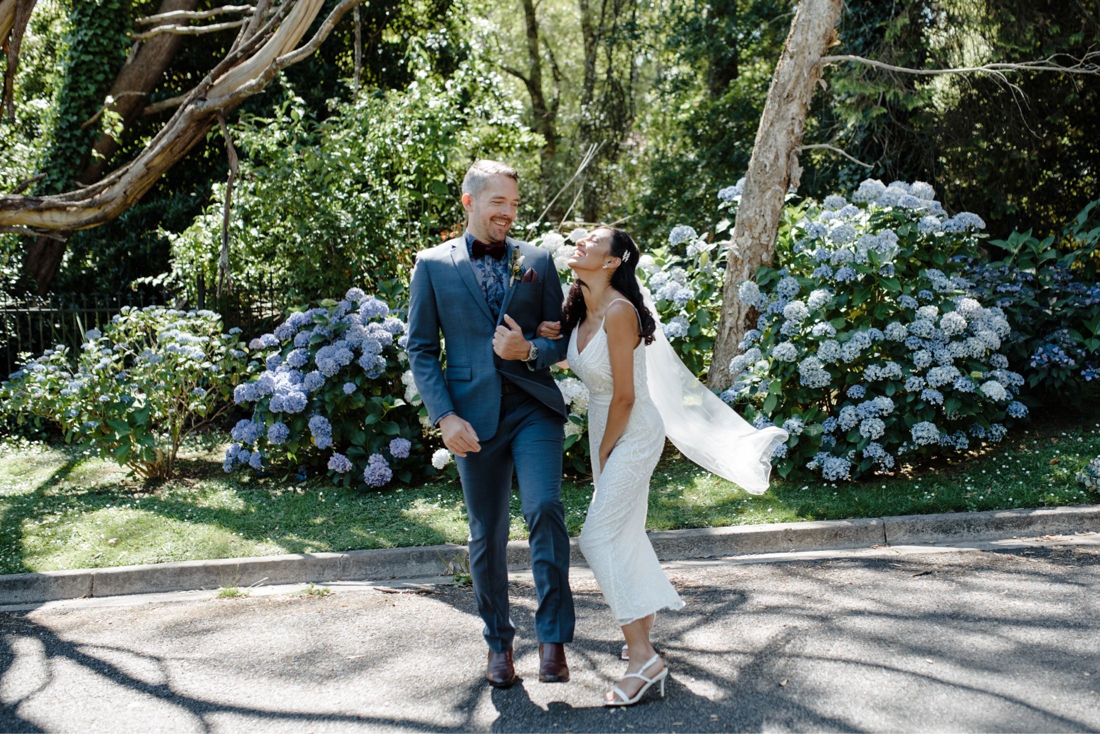 Bride and groom being silly in front of blue hydrangea flowers in Sassafras