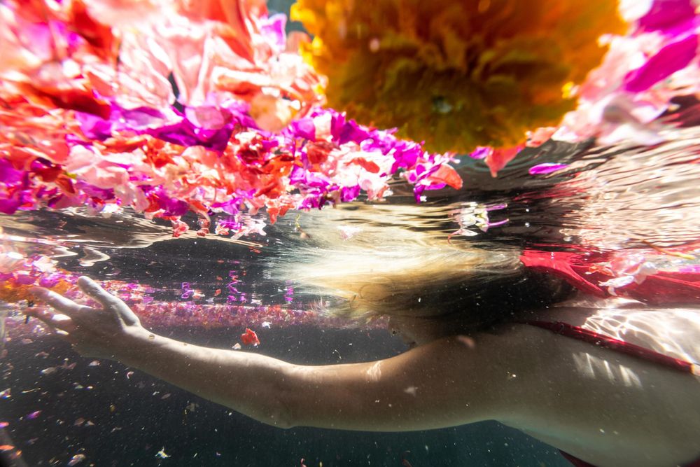 blonde girl reaching for flowers underwater