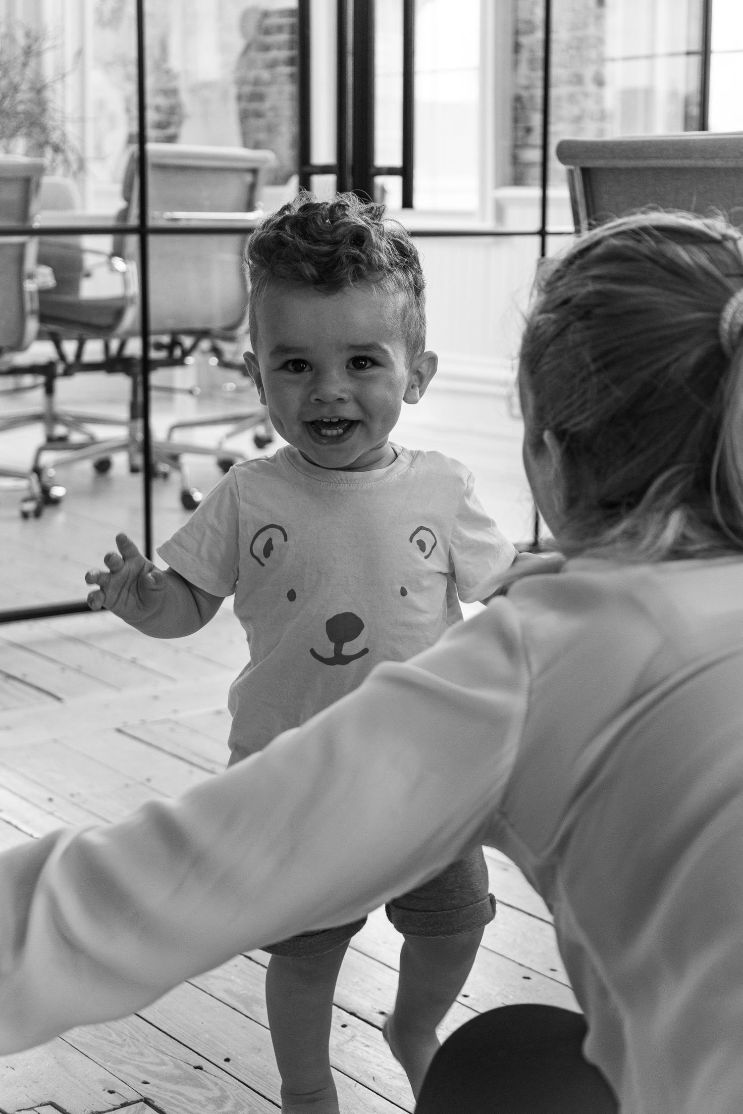Toddler boy walking towards momma's arms with a big smile. Summer hugs and family