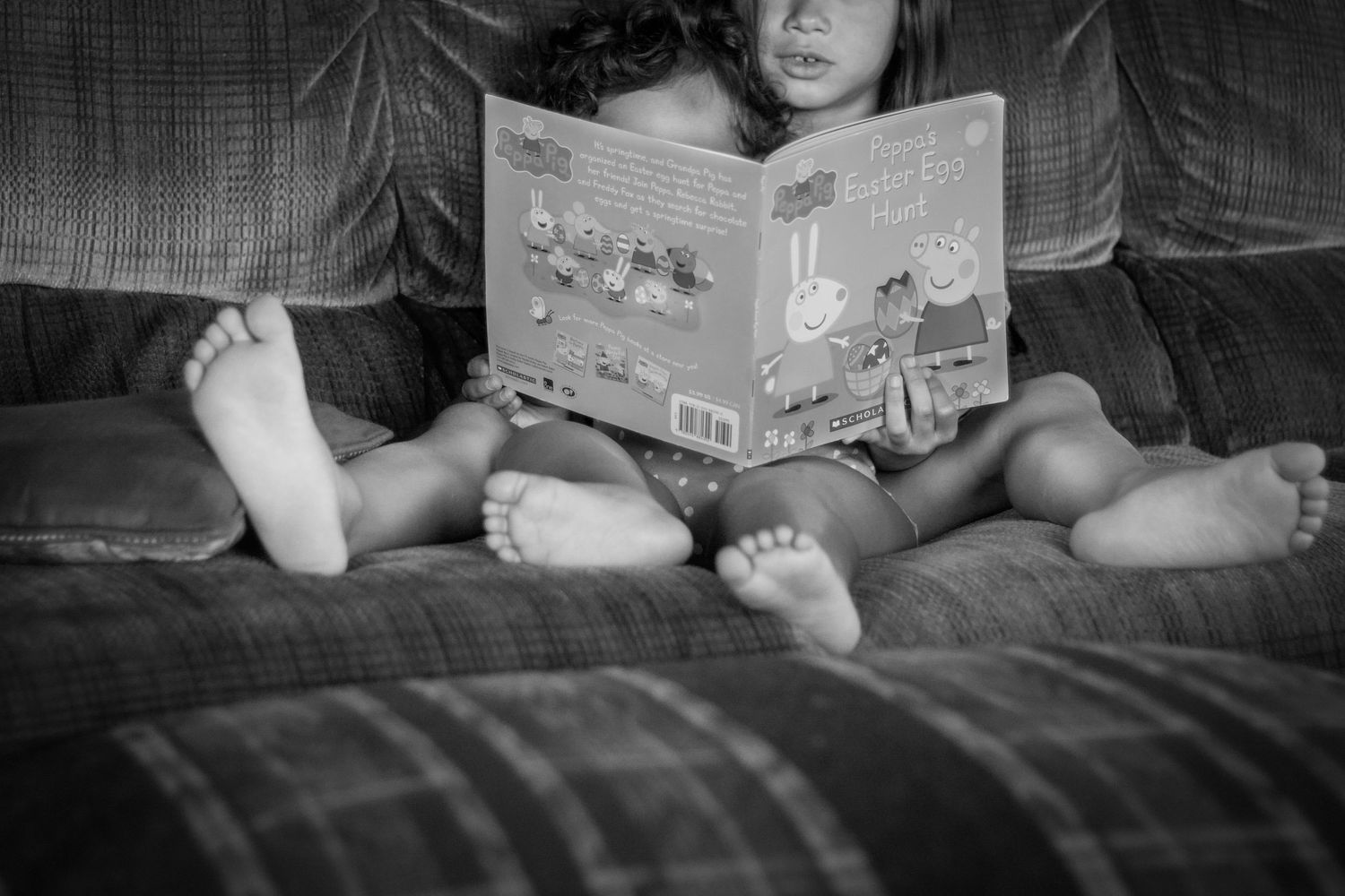 Story time on the couch. Two little girls reading Peppa Pig, and bonding.