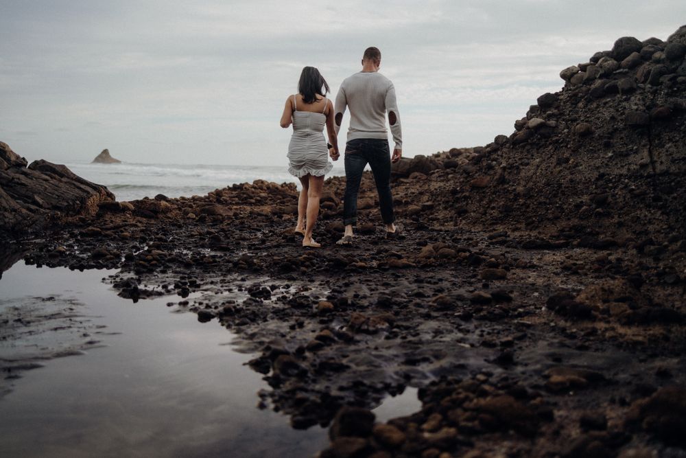 A couple explores rugged coastal rocks during low tide with ocean waves in the background.