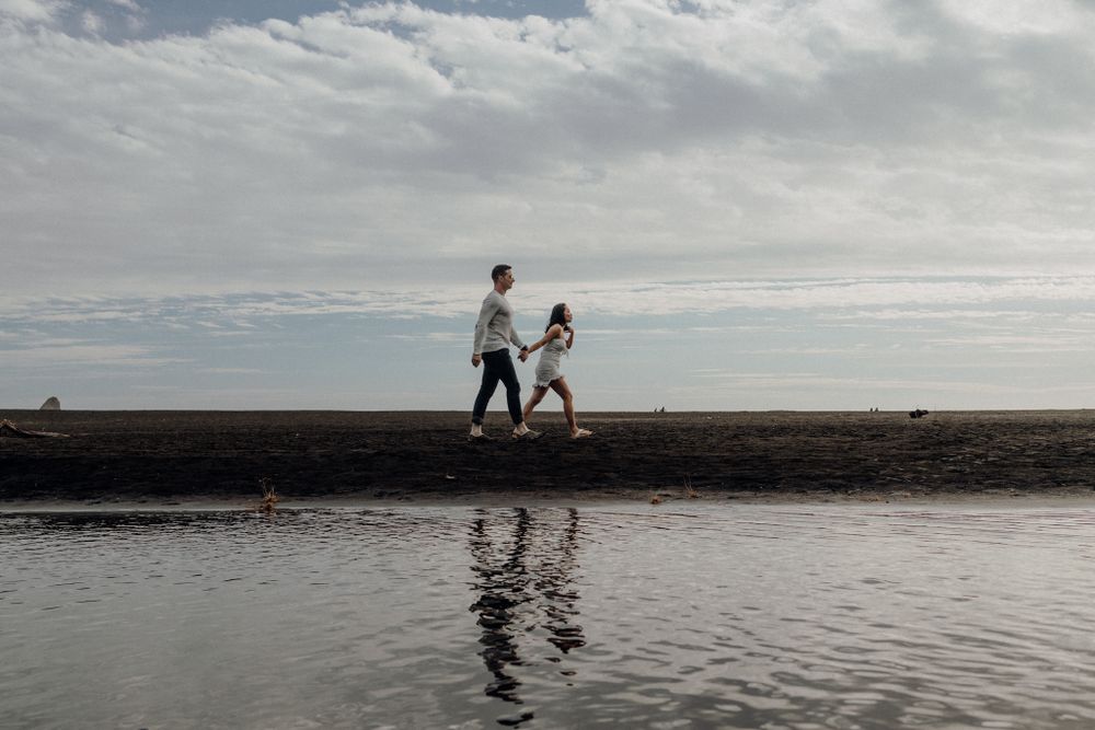 Two silhouettes stand on a jetty with their reflection mirrored in the calm water below.