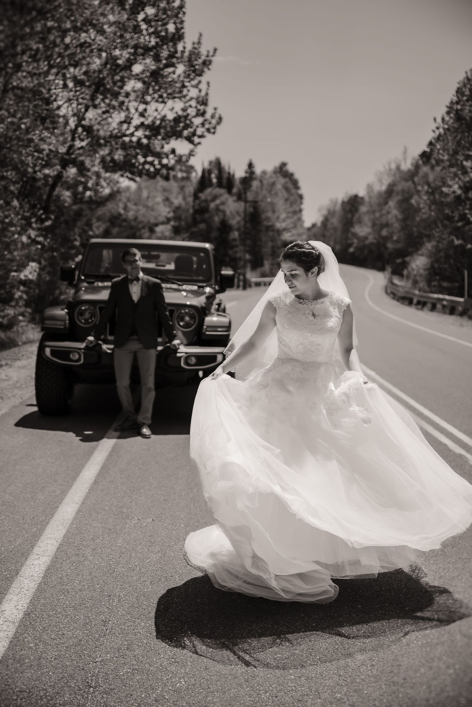 A vintage-inspired wedding photo with a classic car and flowing dress on a country road.