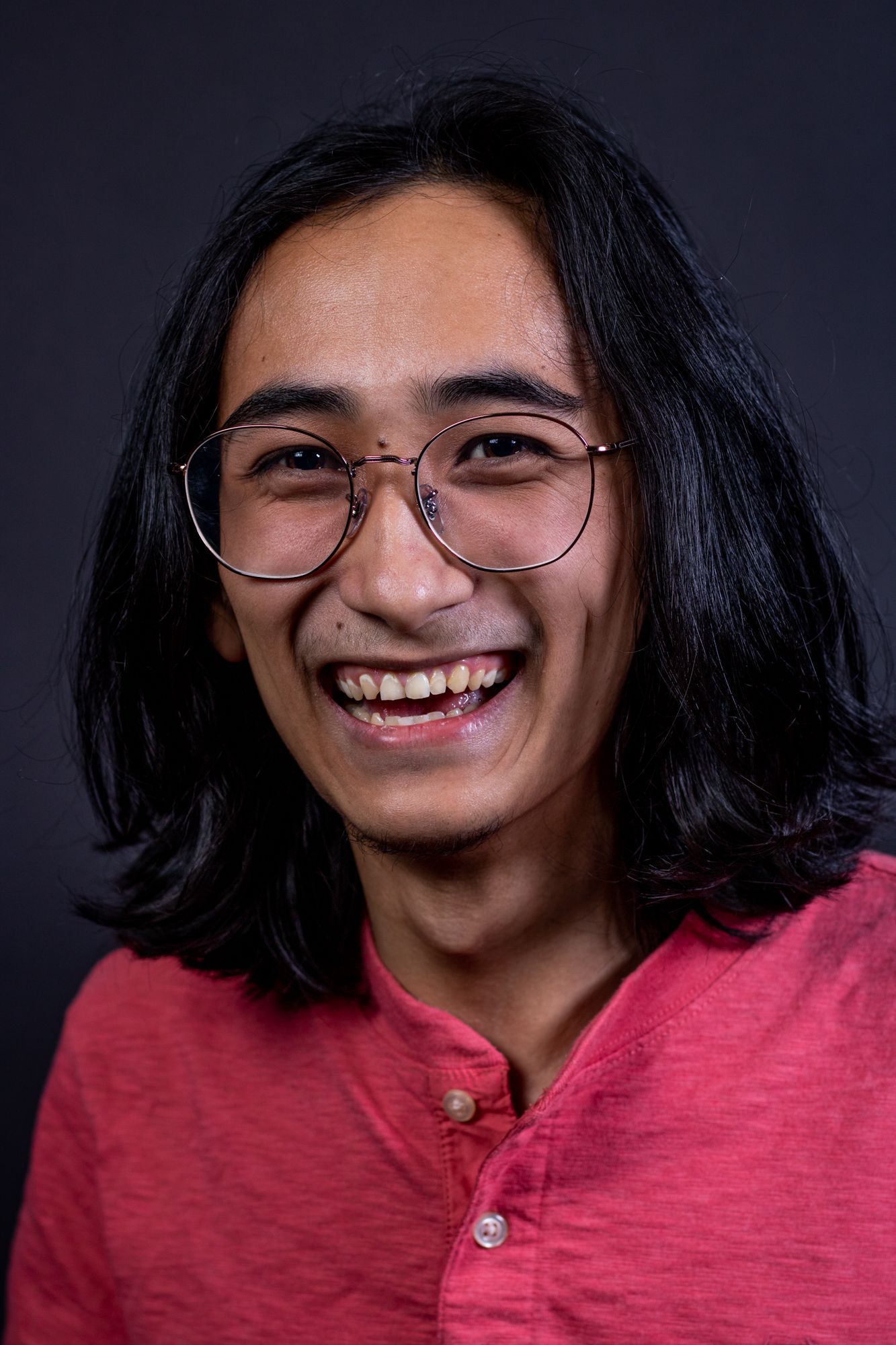 Studio portrait showing person with glasses and long dark hair wearing red shirt.