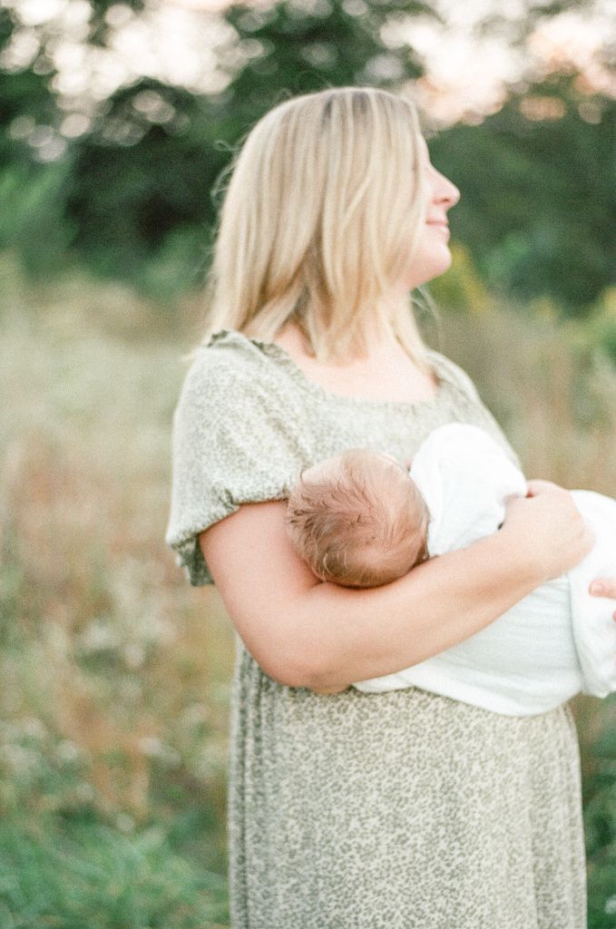 Mother holds her baby in a field at sunset
