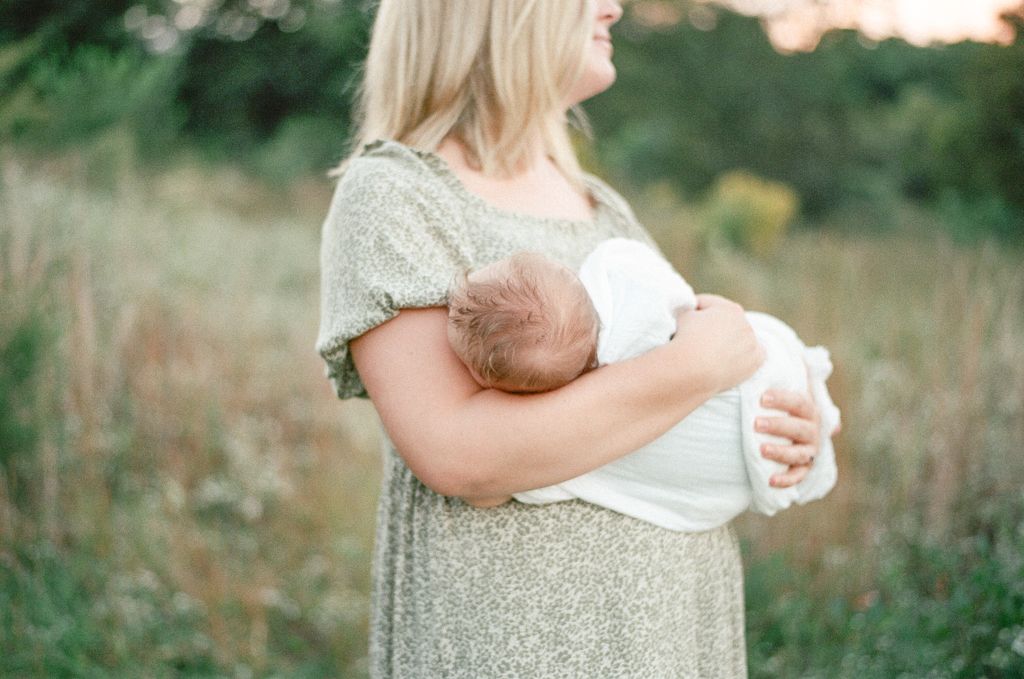 A baby's head rests cradled in her mothers arms as her mother stares off at the sunset