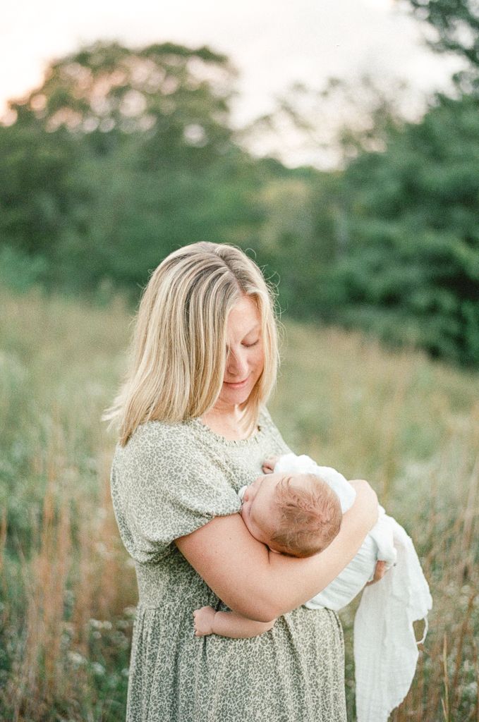 Mother smiles down at her baby as they stand in a field at sunset