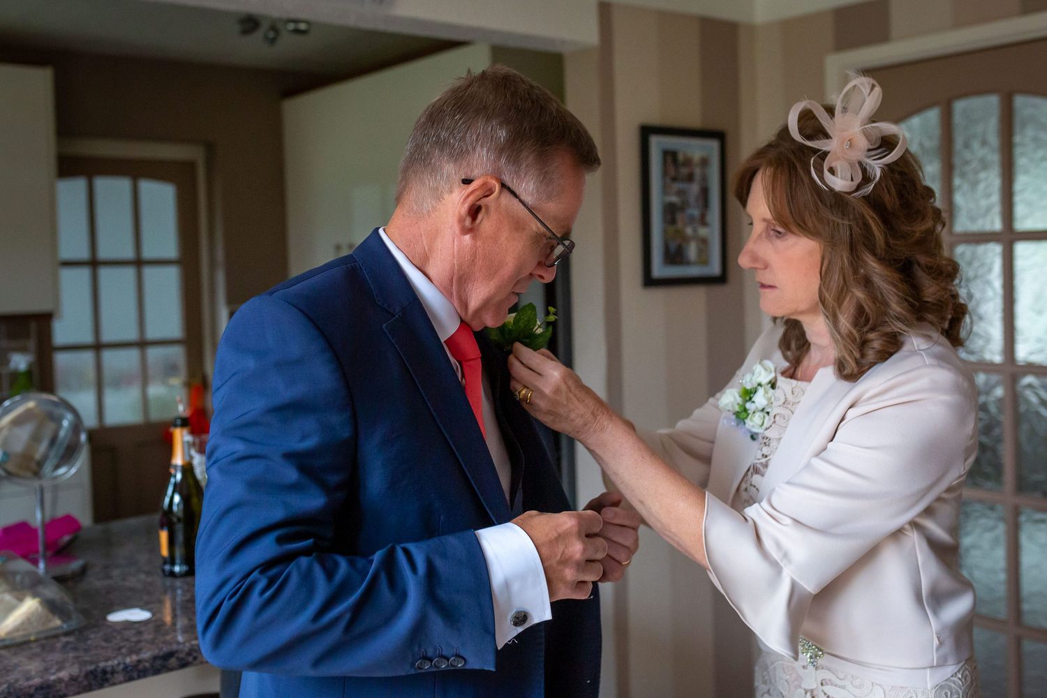 Mother of the bride fastens a button hole flower on her husbands jacket