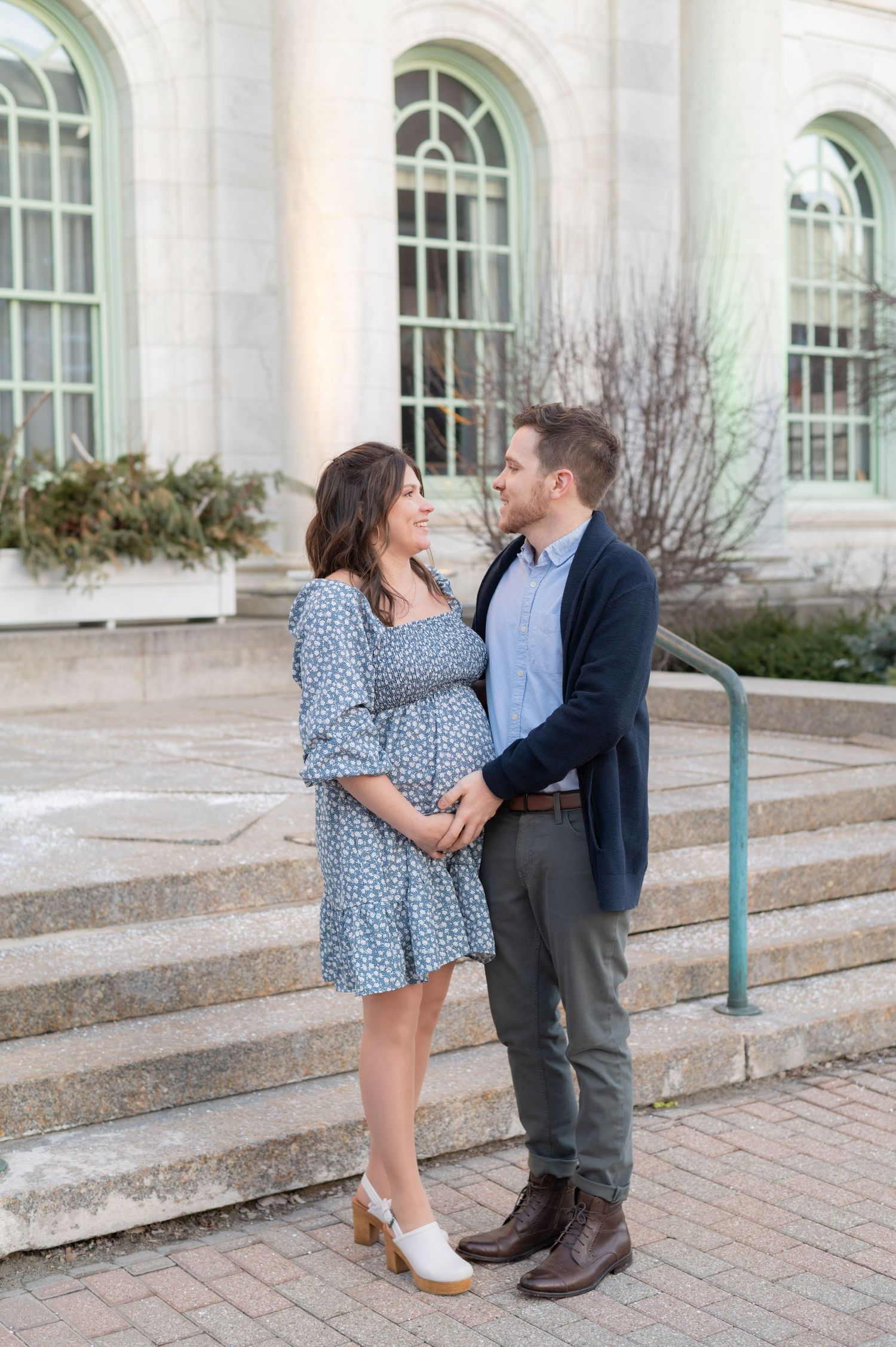 A couple shares a tender moment on stone steps in front of arched windows.
