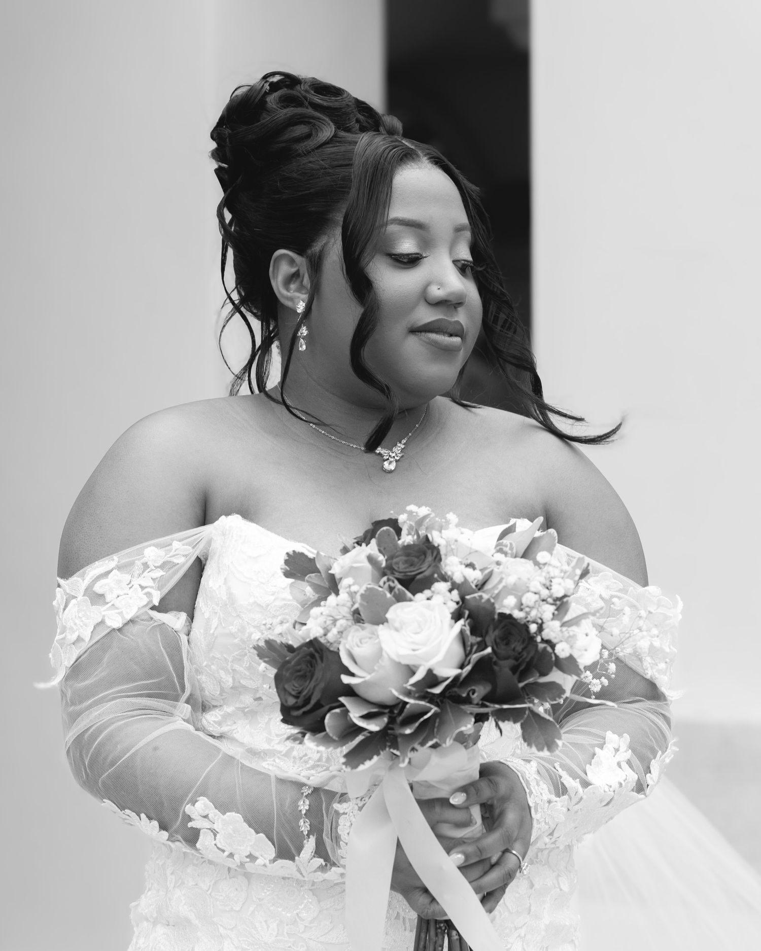 A black and white portrait of a bride with an elegant updo holding her wedding bouquet.