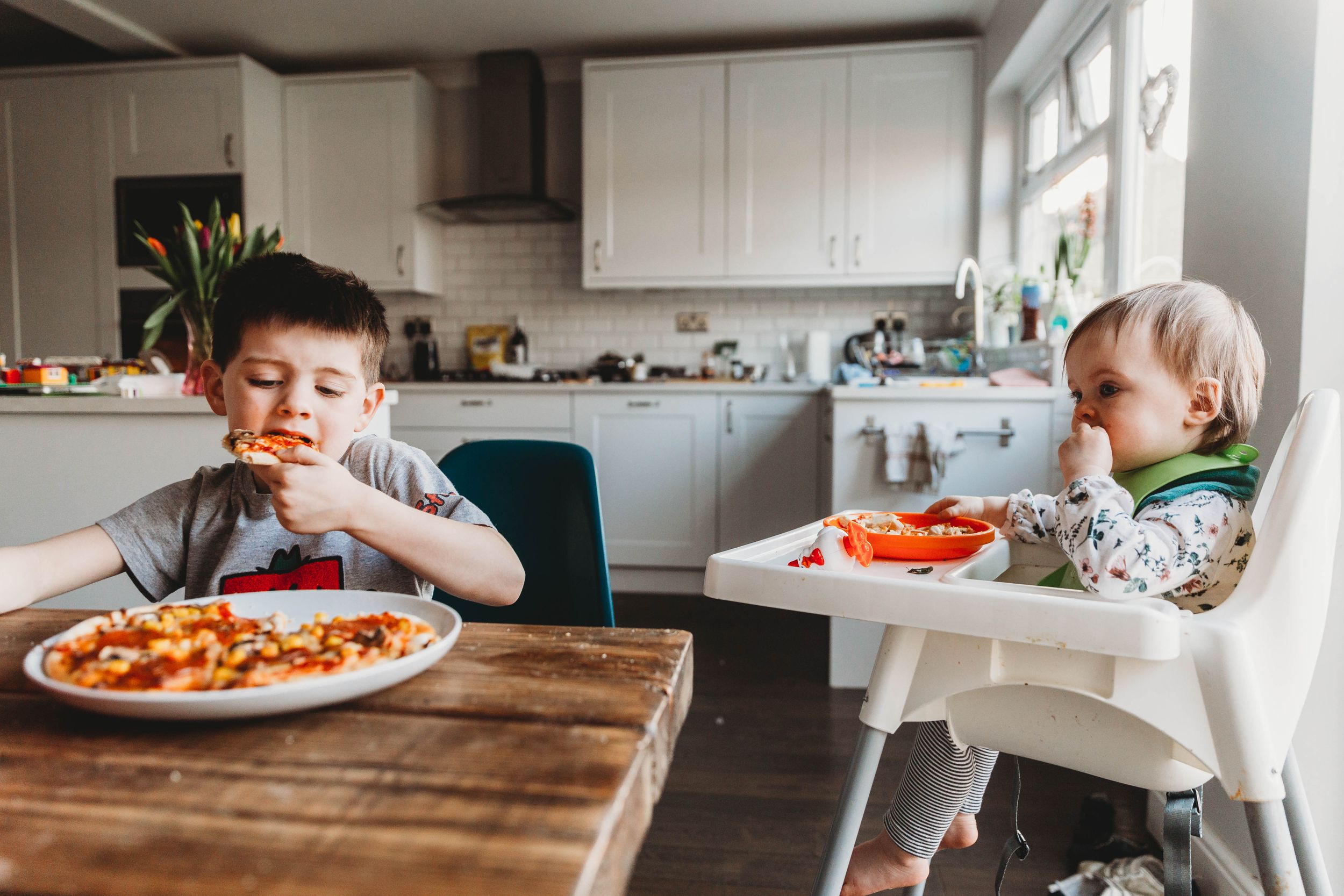 brother and sister eating homemade pizzas in kitchen