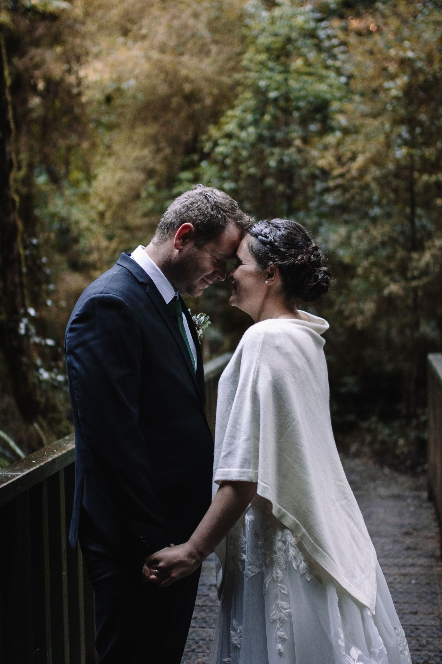 Romantic wedding couple sharing an intimate moment on a forest bridge.