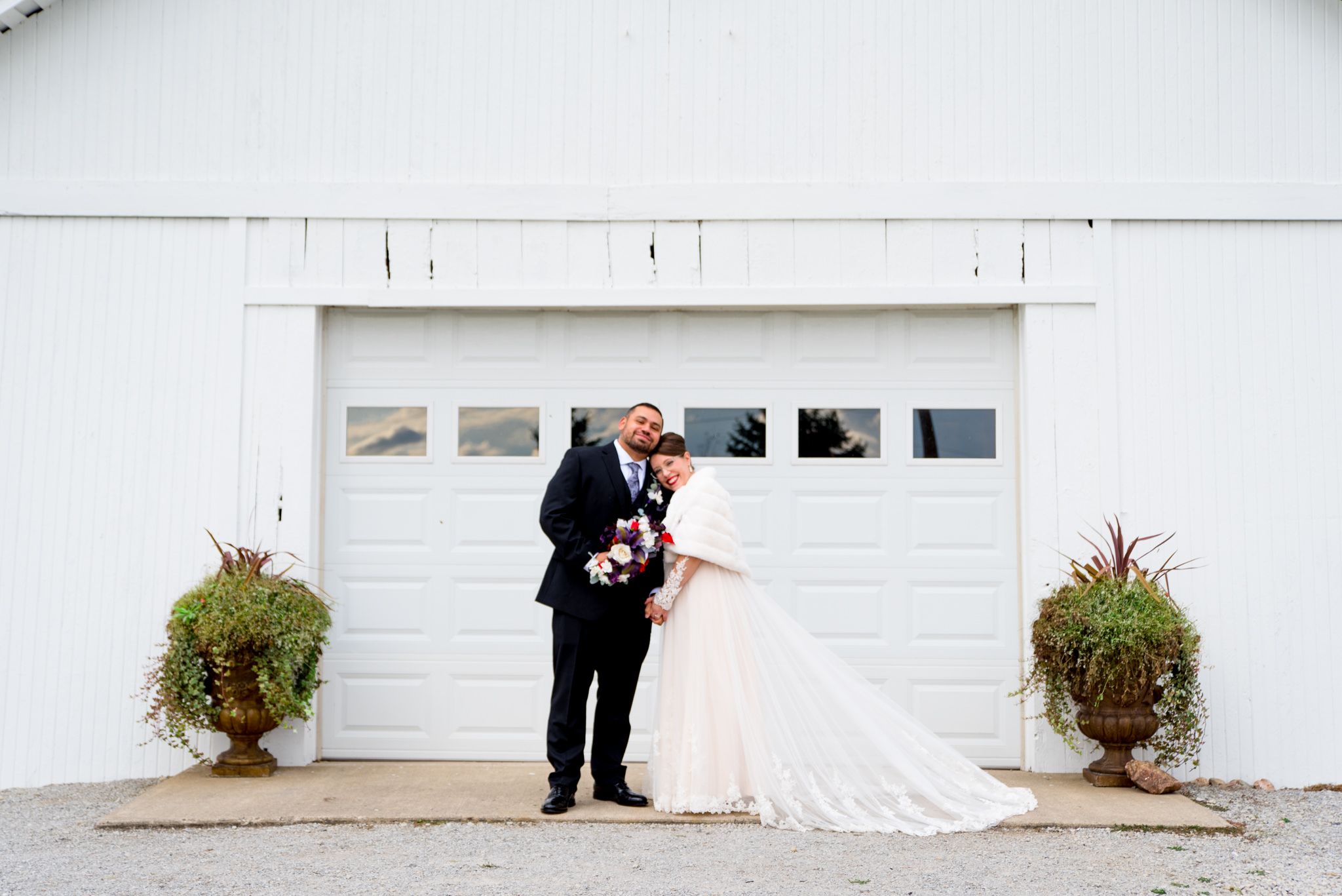 bride and groom snuggling outside white barn