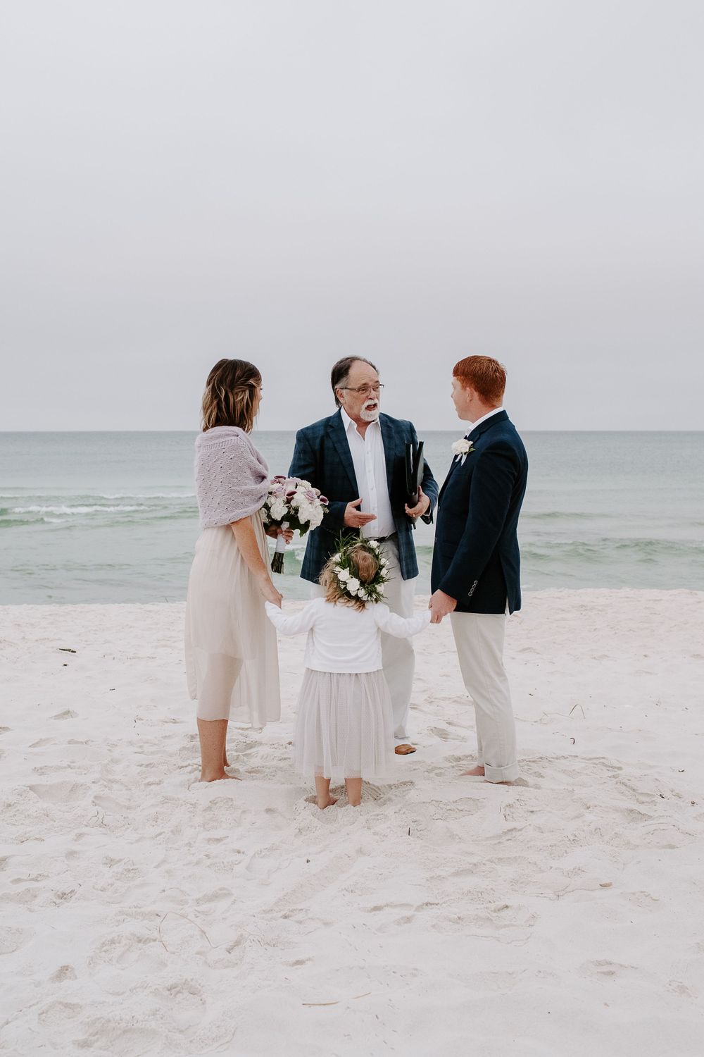 man and woman saying their vows on the beach while their daughter holds their hands