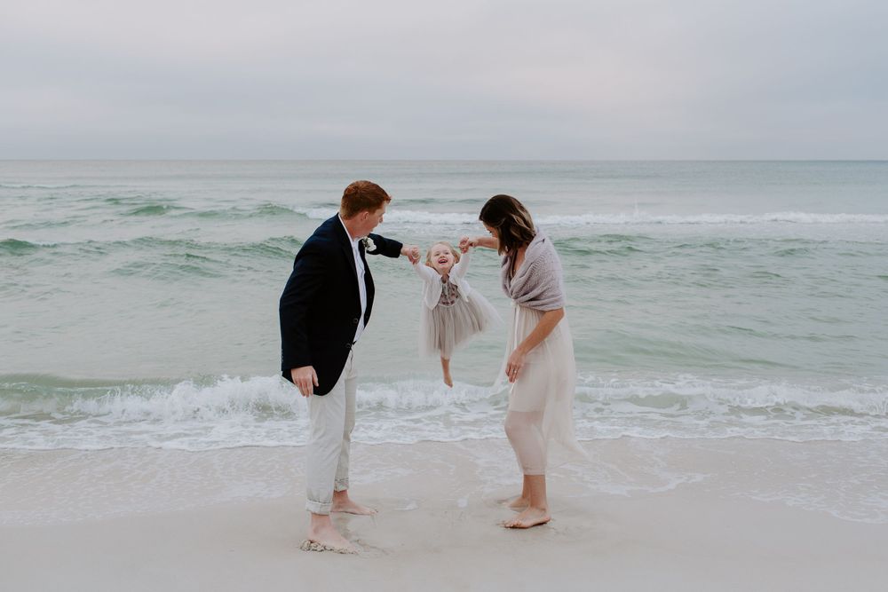 mother and father swinging their daughter after their sunrise beach elopement