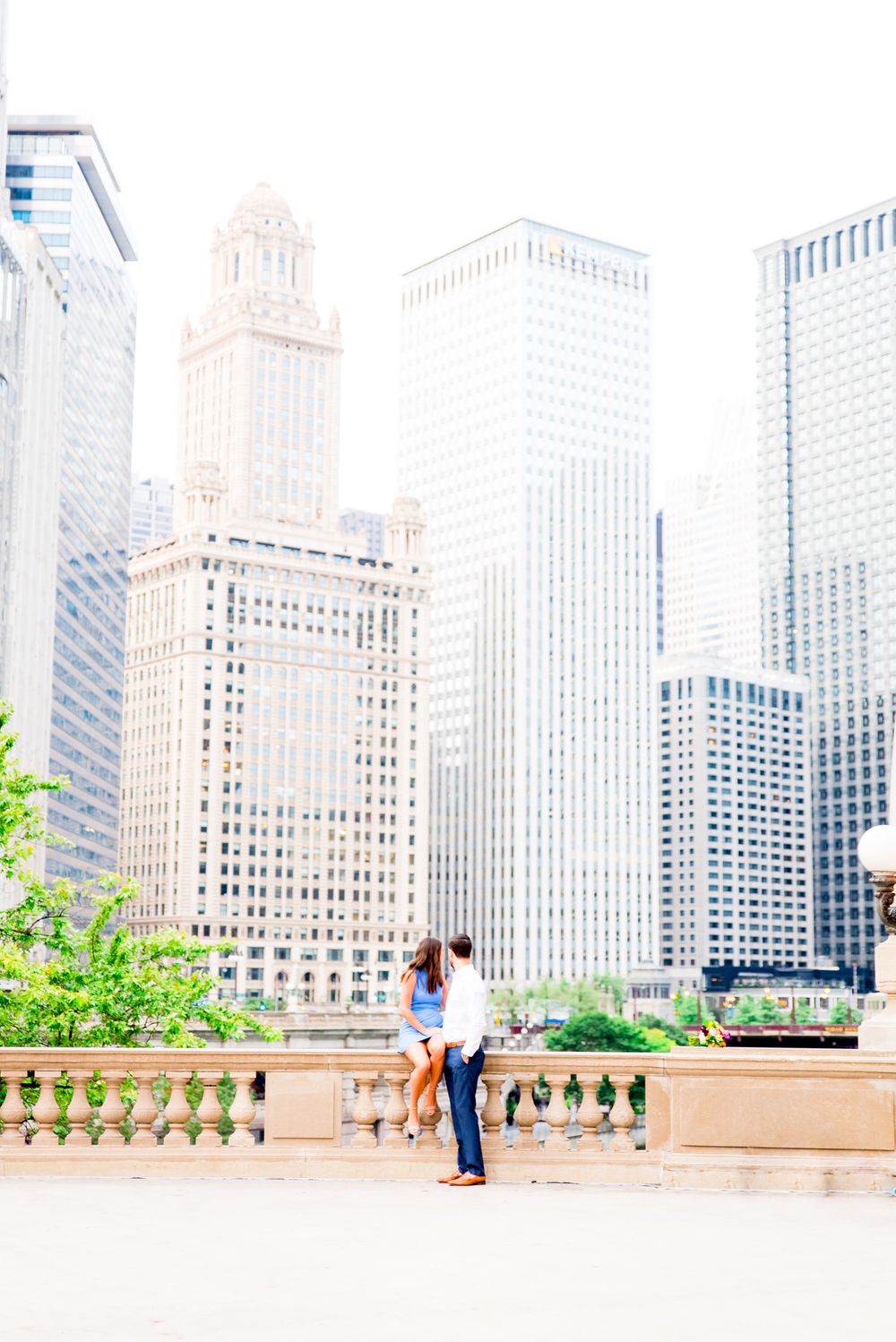 woman with brown hair in blue dress sitting near chicago riverwalk and wrigley building with fiance at sunrise