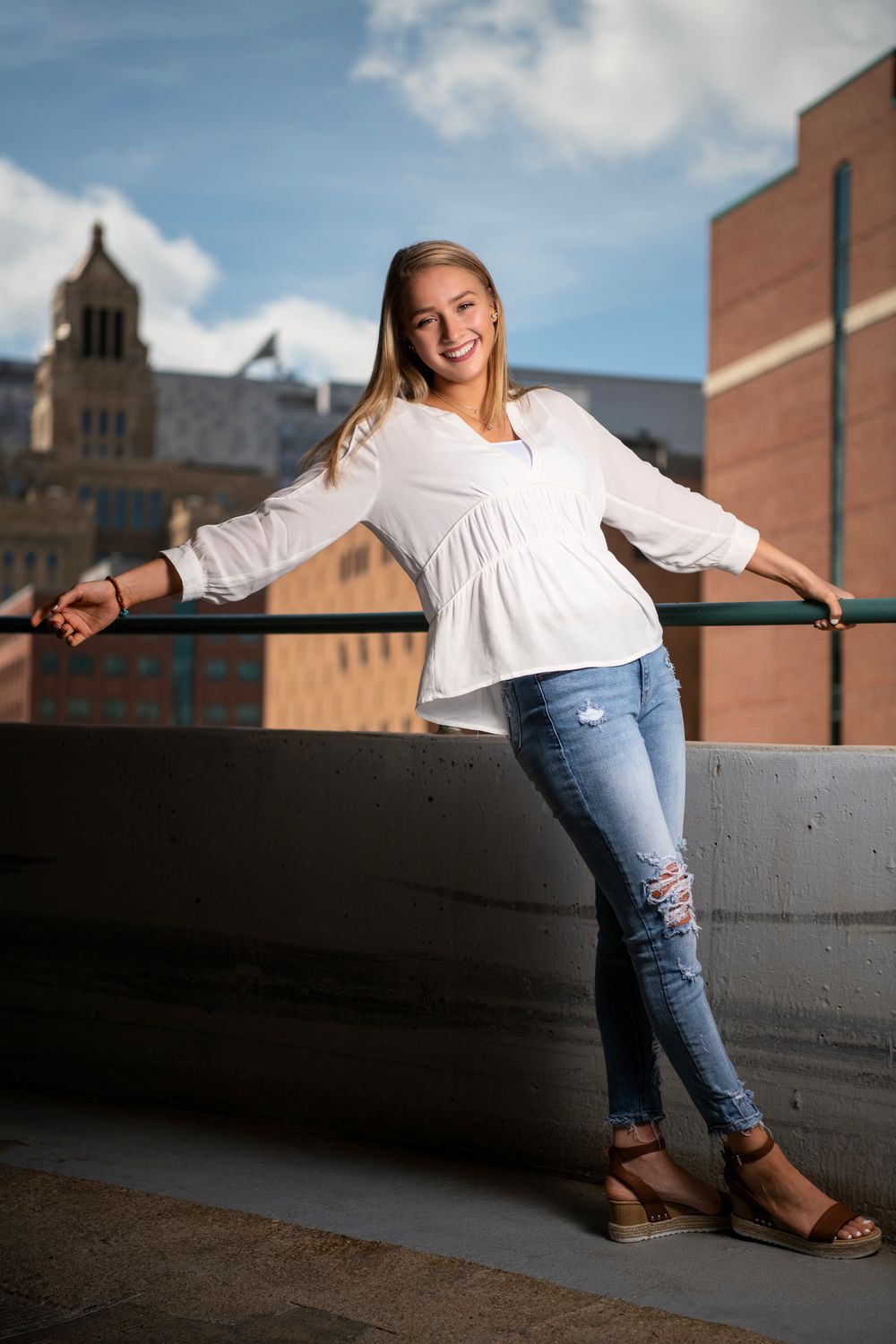 senior girl in white top with torn blue jeans atop parking garage