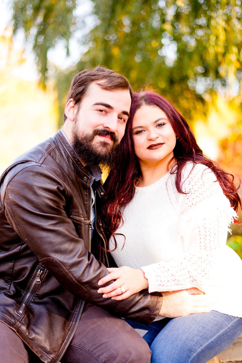 man and woman sit in front of water at Central Park for fall sunrise engagement pictures