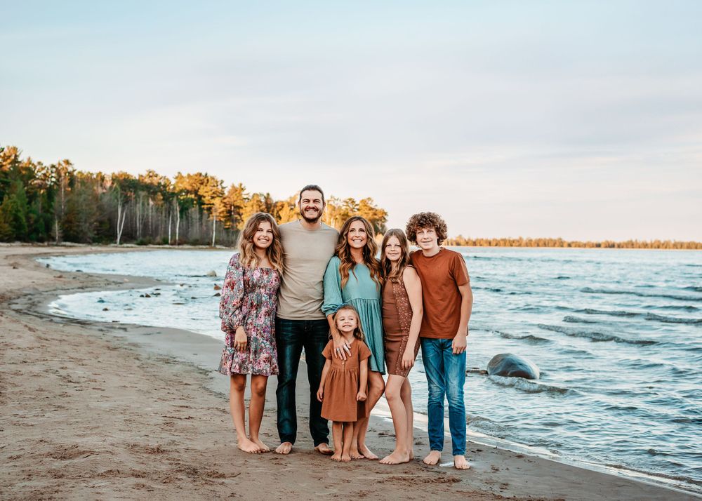 Family standing together on beach at sunset with water and trees in background.