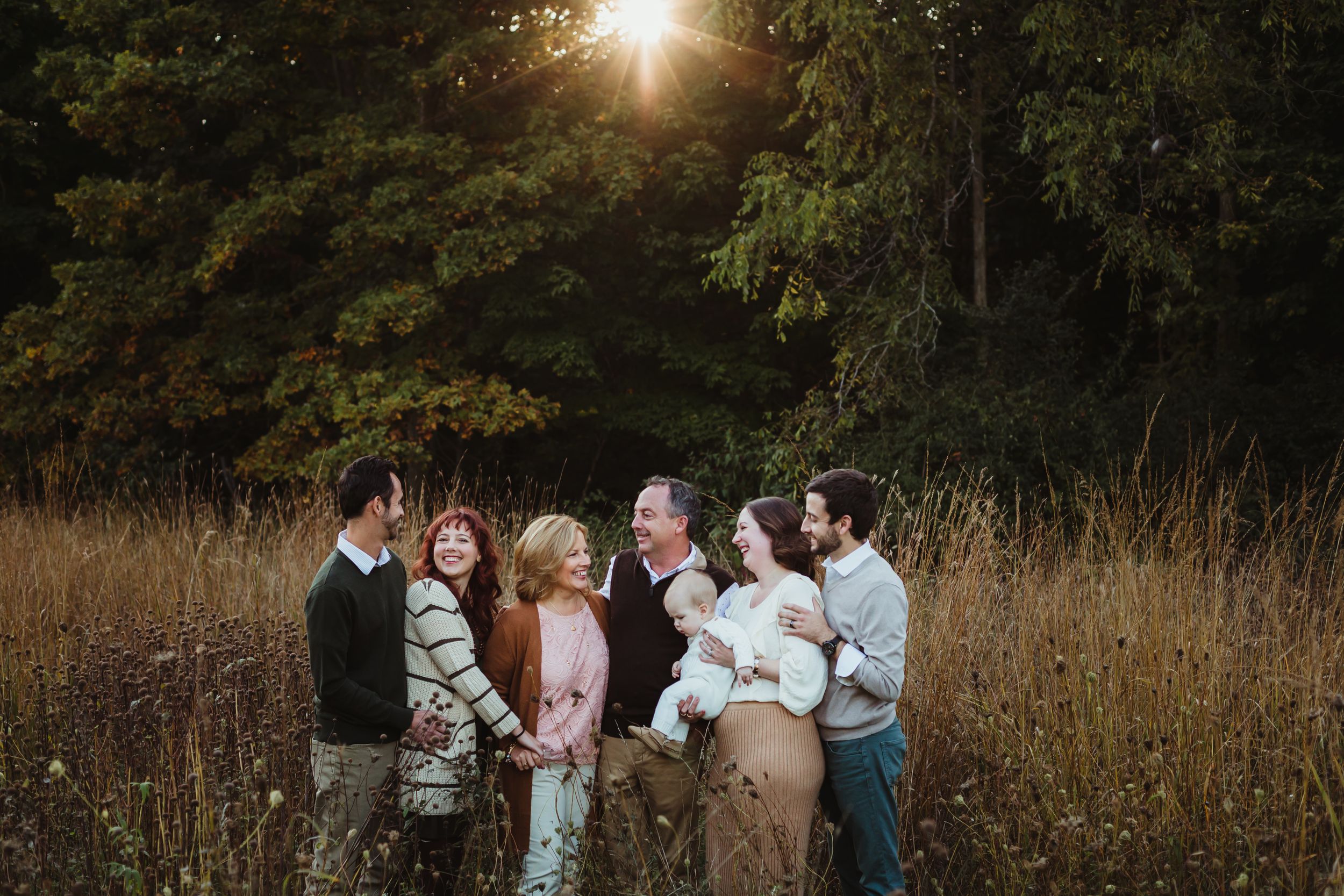 Three generation family photo of everyone laughing in a field.