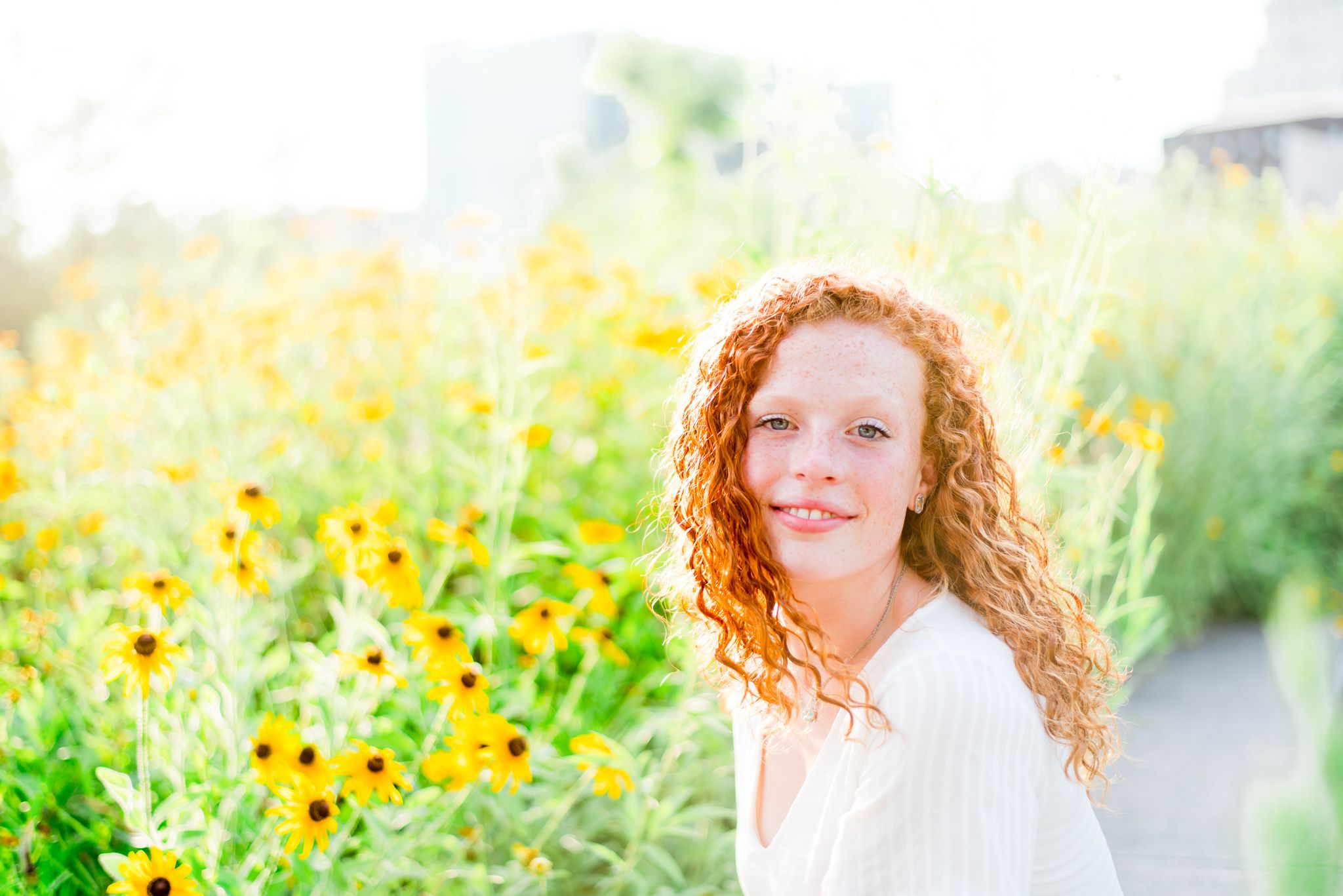 young woman with red curly hair softly smiles in front of black eyes susan flowers in Smale Park