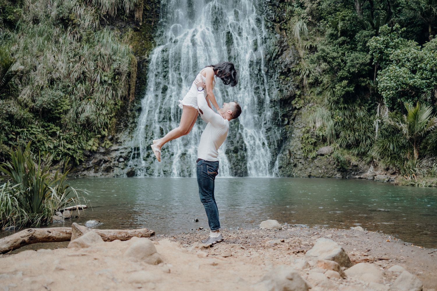 A joyful couple shares a playful moment in front of a scenic waterfall.