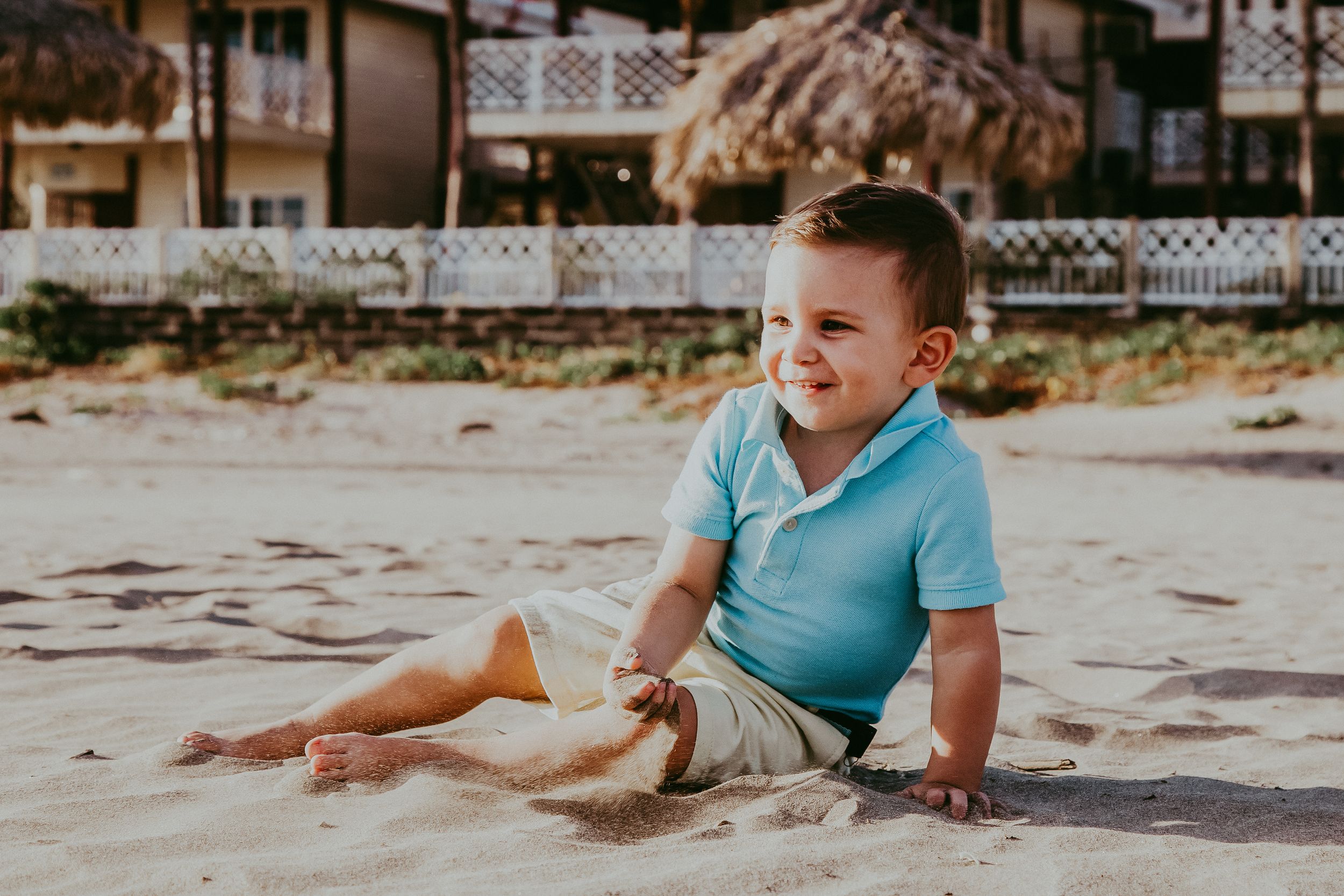 little boy plays in the sand on the beach while looking at the distance
