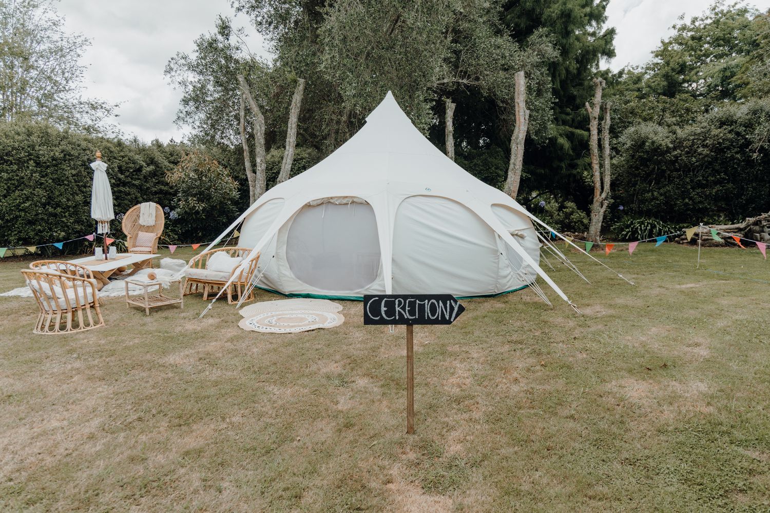A white wedding tent set up on a lawn with wooden chairs arranged for an outdoor celebration.