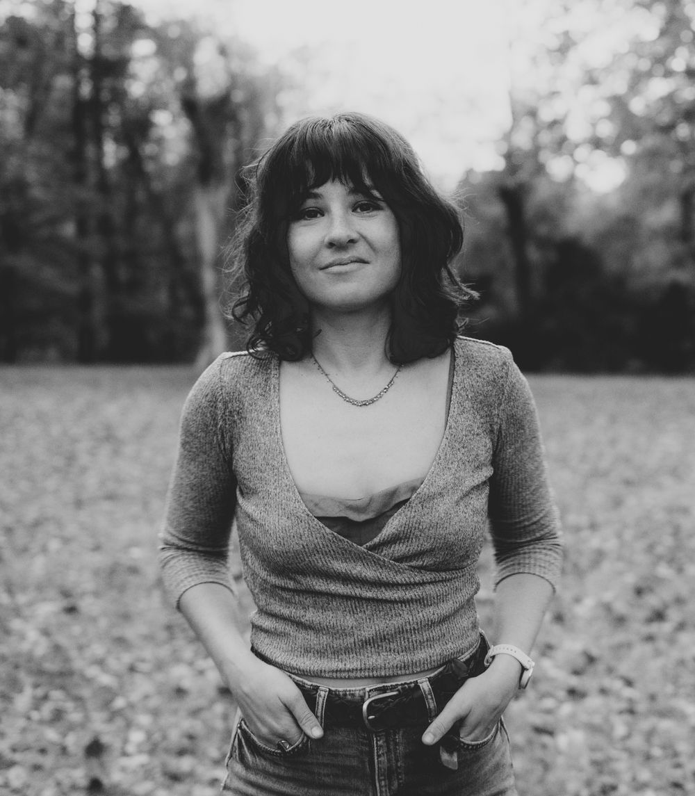 a person standing facing the camera directly and smiling softly in black-and-white in an open field