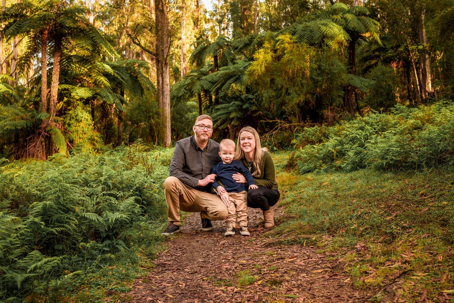 Parents and toddler crouching together on forest path