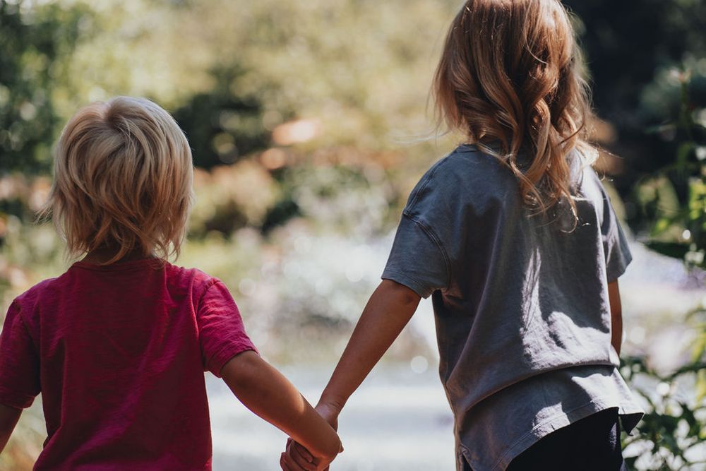 Brother and sister (grandkids) hold hands while watching the fountain in the pond at Sayen Gardens, also spotting coy.